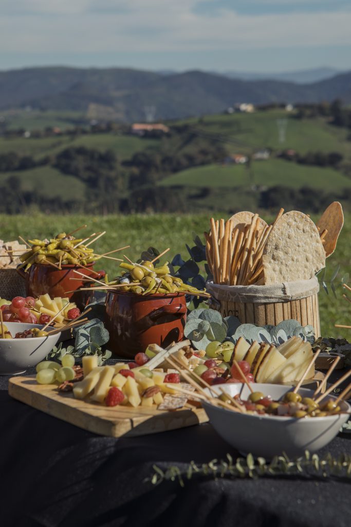 mesa de aperitivos con quesos, frutas y encurtidos en catering de boda Demilarroces en entorno natural en Vitoria